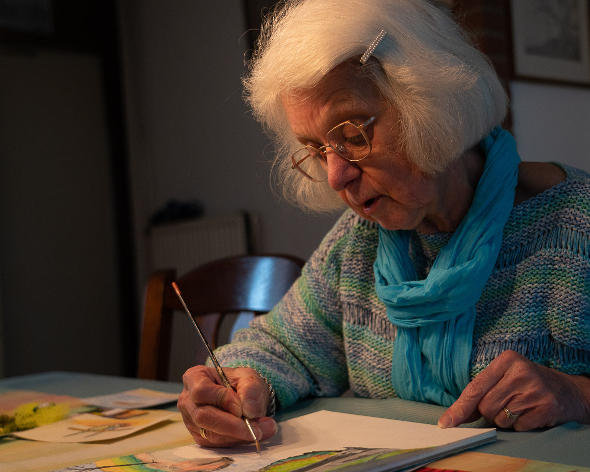Oudere mevrouw schildert aan tafel op papier